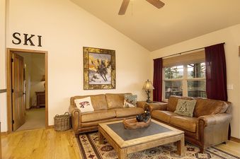 A spacious living room at Rendezvous 45 Reunion Court with two brown leather couches, a wooden coffee table, and a large window offering mountain views.