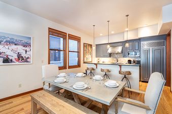 A kitchen and dining room with a large dining table in the foreground and an open kitchen in the background.