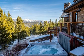 The Latigo Lodge offers a luxurious hot tub with mountain views, surrounded by snowy pines and a rustic log cabin.