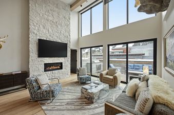 Luxurious living room featuring a grand white stone fireplace, modern furnishings, and large windows with outdoor views.