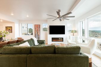 A modern and bright living room at Deer Valley East Above and Beyond with a green sectional, white armchairs, and a cozy fireplace.