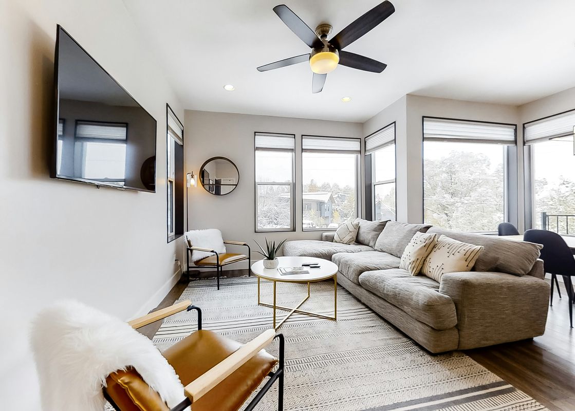 A modern and spacious living room at the Mountain Modern Duplex featuring a large L-shaped sofa, a round coffee table, and large windows with an outdoor view.