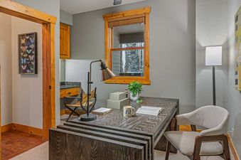 A cozy office space in Starlit Pines Lodge, featuring a wooden desk, a comfortable chair, and a window with a view of the snowy landscape.