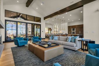 A spacious, modern living room at Sanctuary Chalet at The Colony with vaulted ceilings, large windows overlooking a natural landscape, and comfortable seating.