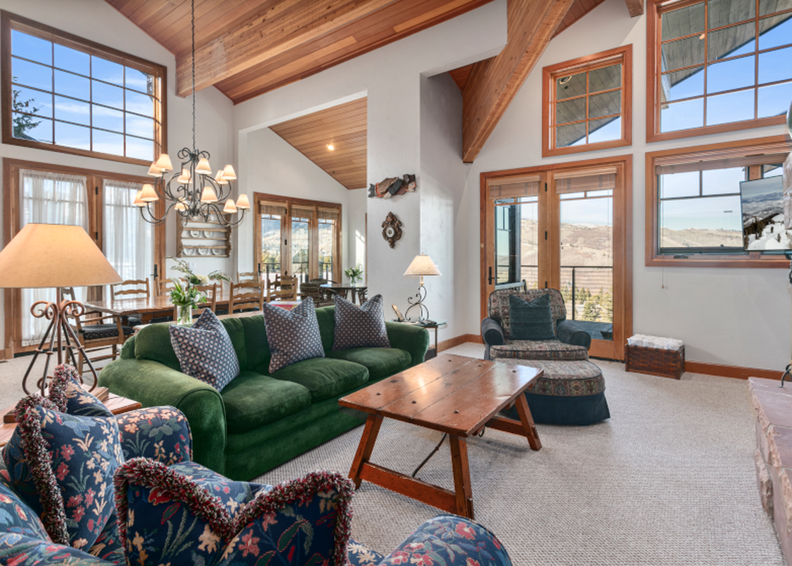 A living room with a green velvet sofa, a coffee table, a fireplace, and large windows with views of the mountains.