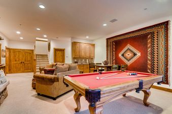 The lounge area at Timber Creek Retreat at River Ridge features a comfortable sofa, a large red pool table, and a built-in wet bar, with a staircase leading upstairs in the background.