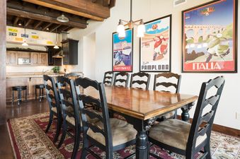The dining area at Silver Star 1305, featuring a large wooden table and chairs, with a view of the kitchen and decorative travel posters on the wall.