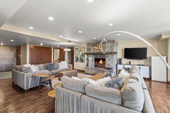 A spacious living room in The Lowell 401 0 features two large sofas, a stone fireplace with a glowing fire, a mounted flat-screen TV, and an elegant arc lamp, all set against a backdrop of rich wooden floors.