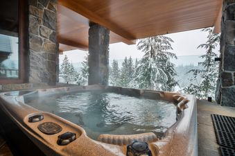 A private hot tub at Totem Chalet, surrounded by snow-covered pine trees and mountains.