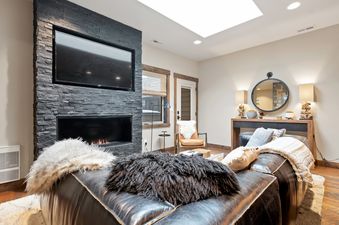 A cozy living room in Central Loft 303 featuring a black leather sofa with plush throws, a modern fireplace, and a flat-screen TV.