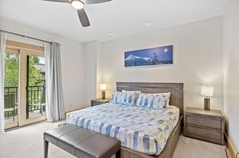 A serene bedroom in Elevation 6000 Condo Unit 99 1 features a king-size bed, elegant wooden furnishings, a private balcony, and a scenic winter landscape painting.