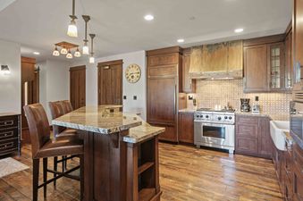 The gourmet kitchen at Arrowleaf Lodge 205 features stainless steel appliances, rich wood cabinetry, and a granite island with seating, illuminated by warm lighting.