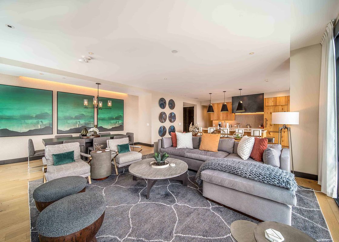 A wide shot of One Snowmass Residence Club 407's open-concept living room, dining area, and kitchen, featuring modern furnishings and vibrant art.
