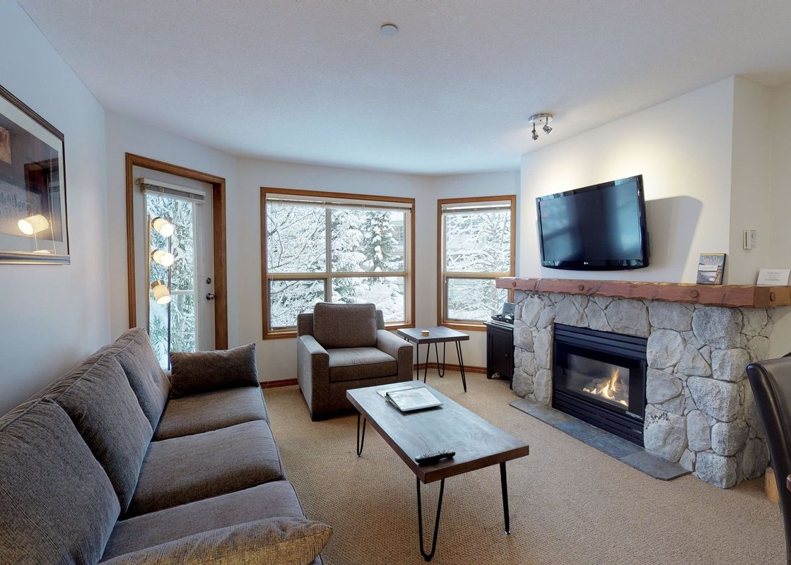 A cozy living room at Aspens on Blackcomb Unit 443 with a warm fireplace, comfortable seating, and snowy outdoor views.
