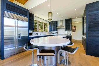 The modern kitchen at Fairway Views Estate At Vail Golf Club boasts a round island with bar seating and stainless steel appliances.
