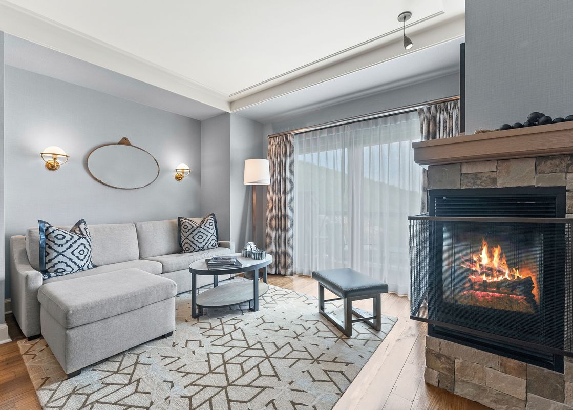 The St Regis Family Valley View Suite living room features a fireplace and a plush sectional sofa, with a large window and patterned curtains.