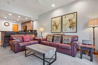 A cozy lounge area in The Charter E2305 featuring two leather sofas with decorative pillows, a coffee table, and an adjacent kitchen with a breakfast bar.