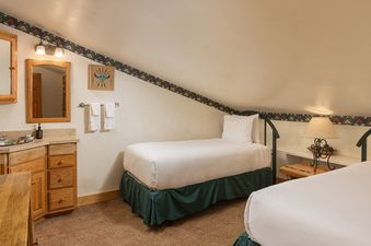 A cozy twin bedroom in Vantage Point 503 featuring two single beds, a vanity with a sink, and an angled ceiling with decorative trim.
