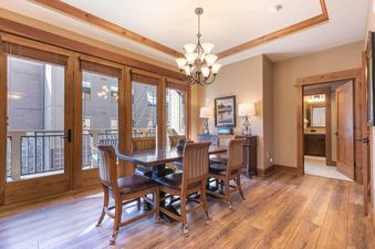A dining room with a wooden table and chairs, a chandelier, and a view of a balcony.