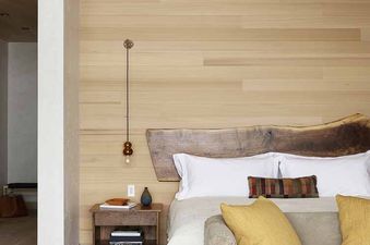 A serene bedroom in the Caldera House Four Bedroom Suite features wood-paneled walls, a live-edge wood headboard, and a cozy gray sofa with yellow pillows.