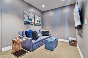 A cozy entertainment area with a blue sofa, ottomans, a wooden side table, wall art, and a mounted flat-screen TV.