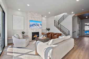 A spacious and modern living room at Deer Valley Modern featuring a fireplace, a television, comfortable seating, and a staircase leading to an upper floor.