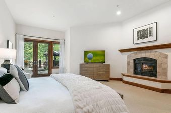 The master bedroom at Centennial Vista features a plush king-sized bed, a fireplace, a television, and french doors that open to a balcony.