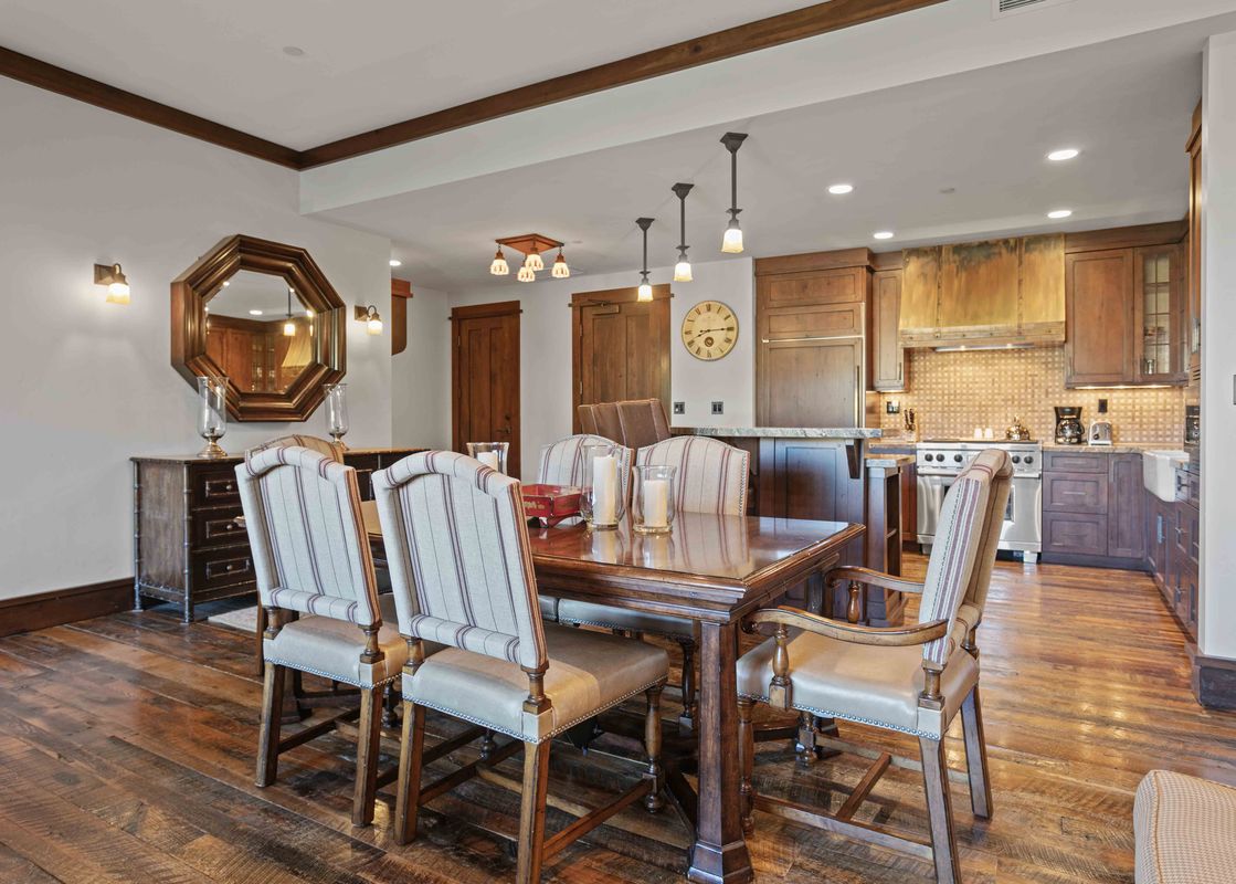 The dining area and kitchen in Arrowleaf Lodge 205, featuring a dark wood dining table with upholstered chairs, and a kitchen with wooden cabinetry and modern appliances.