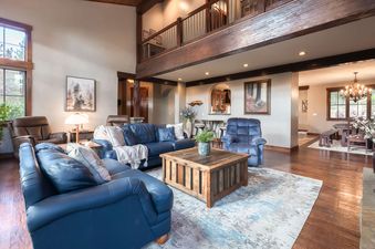 A spacious and elegant living room in the Back 9 Lodge featuring navy blue sofas, a rustic wooden coffee table, and a lofted area above.