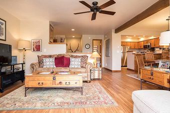 An inviting open-concept living area at Ranch at Steamboat RA307 featuring a comfortable sofa, flat-screen TV, rustic wooden coffee table, ceiling fan, and views into the kitchen and dining area.