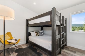 A modern children's bunk room at Quarry A40 with a dark wood bunk bed, a yellow butterfly chair, and a window revealing a scenic mountain view.