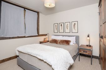 A serene bedroom at Mountain Lake Condo 101B featuring a queen-size bed with white bedding, flanked by nightstands with lamps, and decorated with feather artwork above the bed.