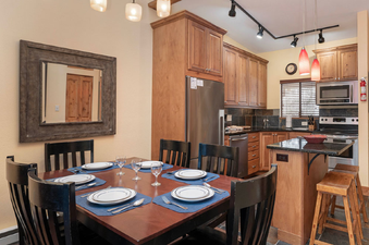 A dining table with place settings sits next to a kitchen with wooden cabinets and stainless steel appliances at Beaver Village 333.