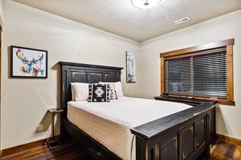 The bedroom of Baker Loft 302 showcasing a distressed black wooden bed with white quilted bedding, colorful deer art, and a window with wooden blinds.