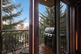 A private balcony at The Charter E340 features a BBQ grill and outdoor seating, surrounded by pine trees with mountain views.