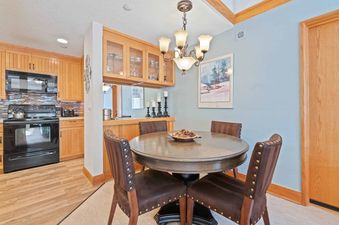 A cozy dining area with a round wooden table and four brown leather chairs, next to a kitchen with light wood cabinets and black appliances.