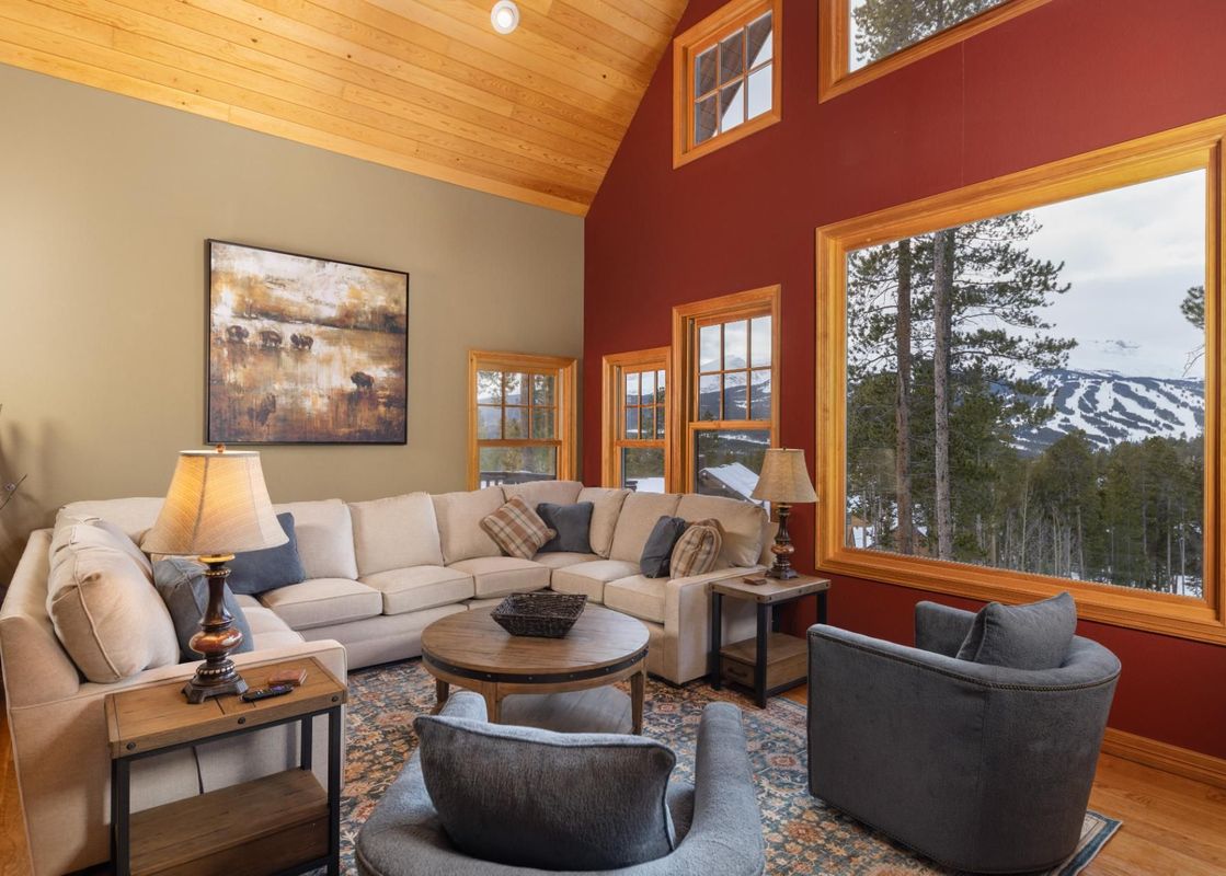A spacious living room with large windows overlooking snowy mountains.