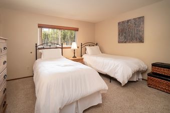 Two twin beds with white duvets and pillows sit side-by-side in a carpeted bedroom at Beaver Village 1624, bathed in natural light from a large window.