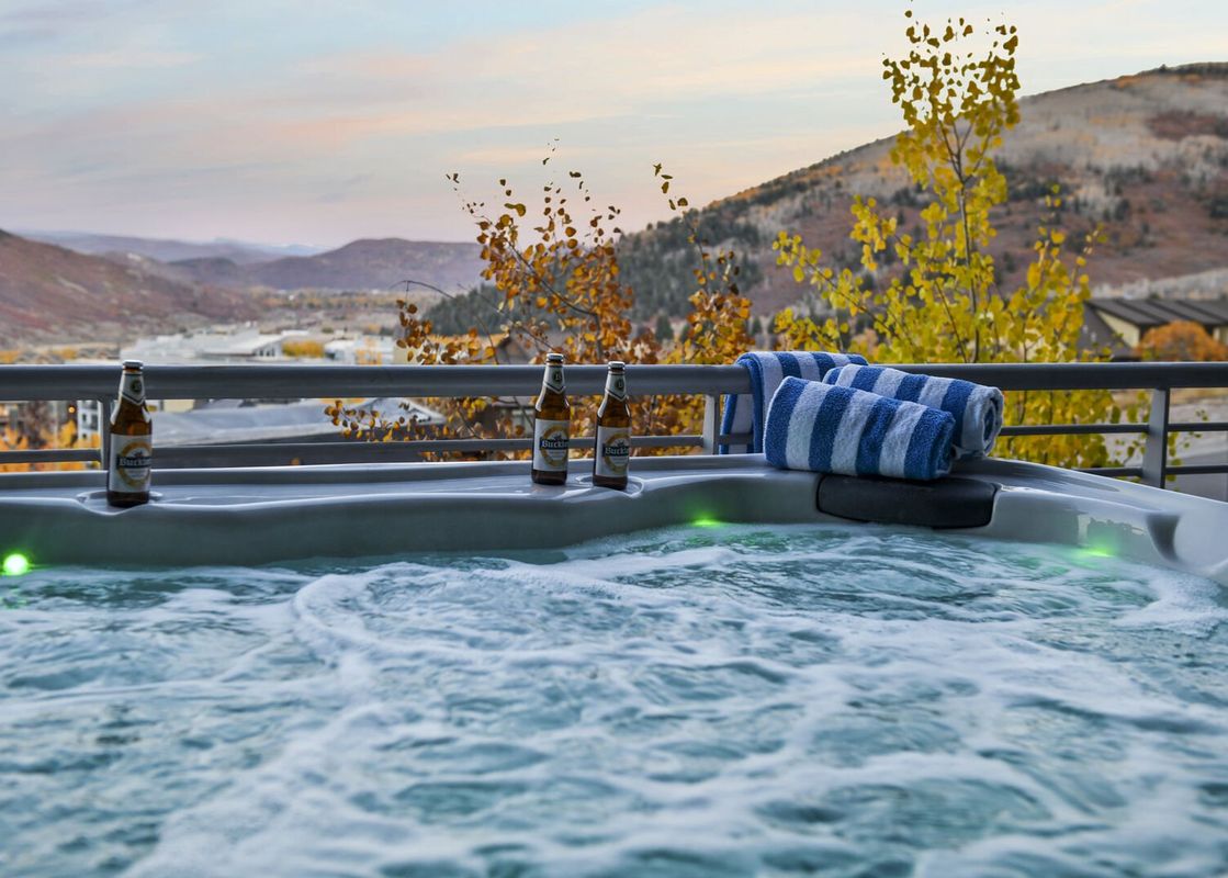 A bubbling hot tub on a private balcony at Apex 1501, offering panoramic views of a vibrant autumn mountain landscape under a twilight sky.