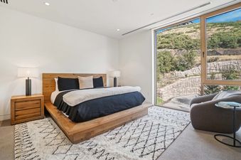 A modern bedroom in Founders Place 1701 with a wooden platform bed, black and white bedding, two bedside lamps, and a large window overlooking a natural hillside.