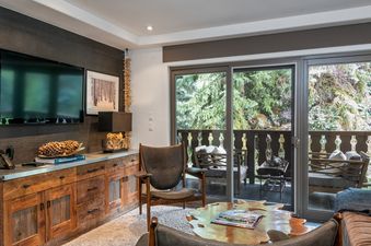 The living area of the Bridge Street Lodge 2 Bedroom Diamond Unit 306 features a rustic wooden cabinet, a comfortable chair, and a large glass door leading to a balcony.