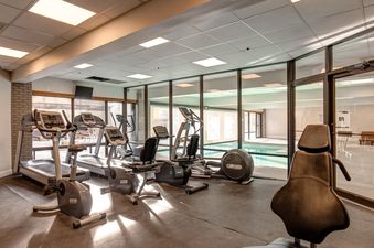 A bright fitness center at Resort Plaza 5051 with various exercise machines and a view of an indoor pool through large glass windows.