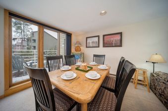 A dining area with a wooden table set for six, black chairs, and a large window showing a snowy outdoor view.