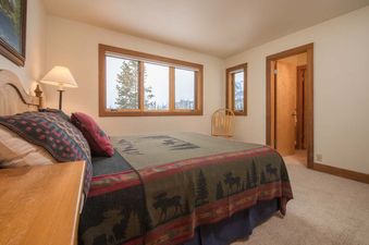 A rustic bedroom in Nez Perce C4 with a mountain-themed bedspread and windows showing snowy outdoor trees.