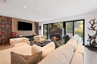 A luxurious living room at The Charter L022 featuring a fireplace, a large L-shaped sofa, and armchairs, with a view of Aspen trees through the windows.