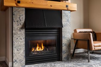 A close-up view of the fireplace in The Westin Resort Deluxe Studio Suite Mountain View, featuring a natural stone facade and a warm, glowing fire, with a cozy armchair visible to the right.