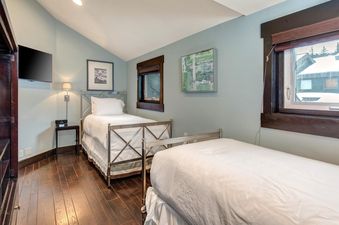 A cozy twin bedroom in Lakeside 1629 featuring two single beds with white linens, hardwood floors, a wall-mounted TV, and serene blue walls.