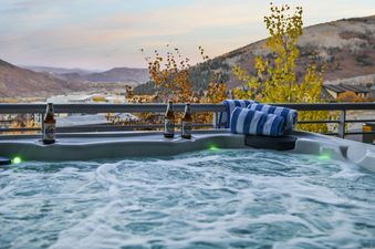 A bubbling hot tub on a private balcony at Apex 1501, offering panoramic views of a vibrant autumn mountain landscape under a twilight sky.