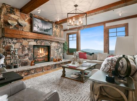A cozy living room in Grand Lodge Three Bedroom Deluxe 407 with a fireplace, comfortable furniture, and stunning mountain views from the large windows.