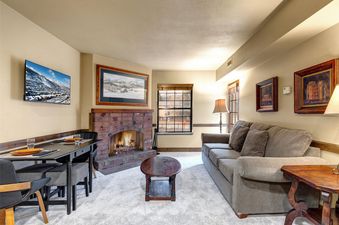A cozy living room at Copperbottom Inn 202 with a gray sofa, a wooden coffee table, a brick fireplace, and a dining area.